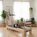 Pilates reformer in a bright room with light coloured flooring and greenery.