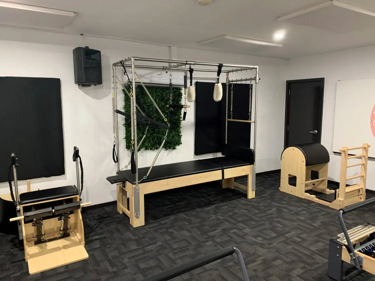Wooden Cadillac Table with black upholstery in a studio with other Pilates equipment. Many attachments are included with the table.