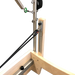 Close up of pilates reformer showing light wooden frame and metal trapeze attachment.
