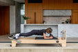 Person using light coloured wood pilates reformer in kitchen.
