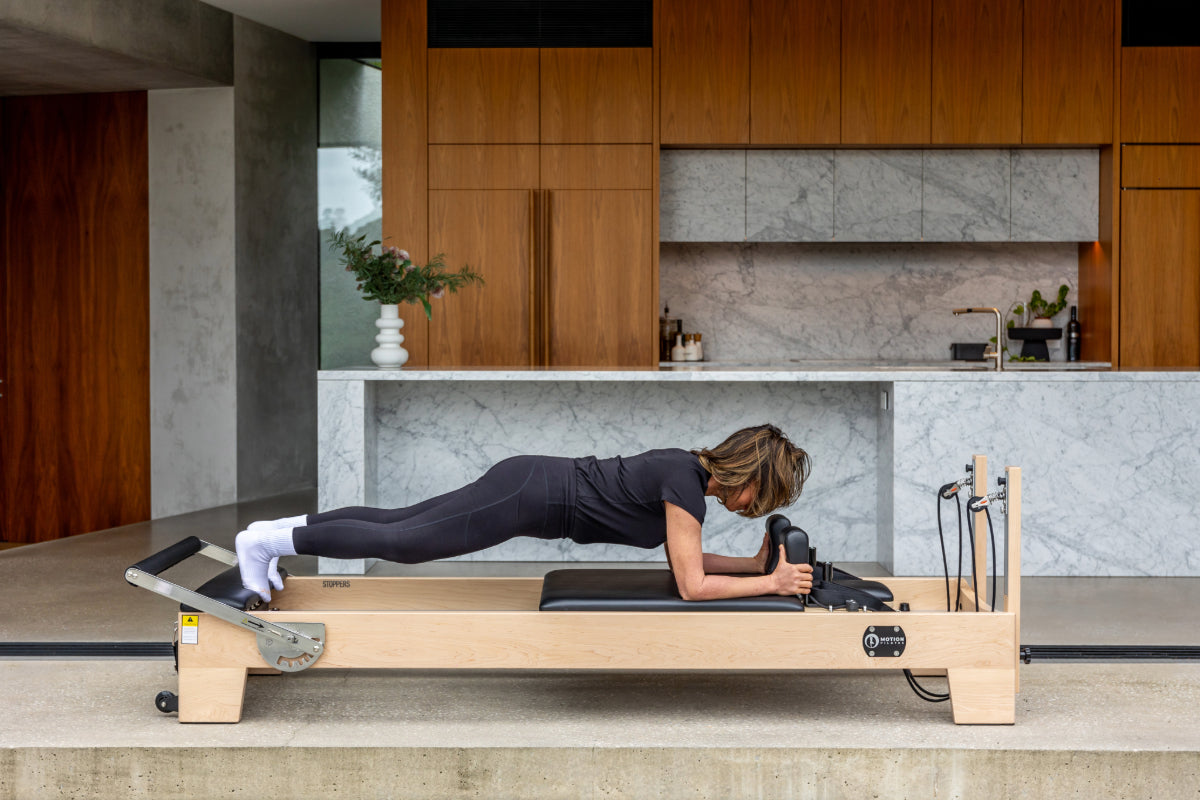 Person using light coloured wood pilates reformer in kitchen.