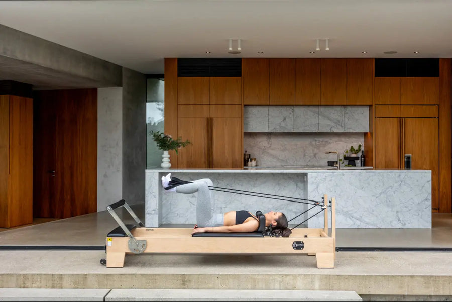 Person using light coloured wood pilates reformer with black upholstery.