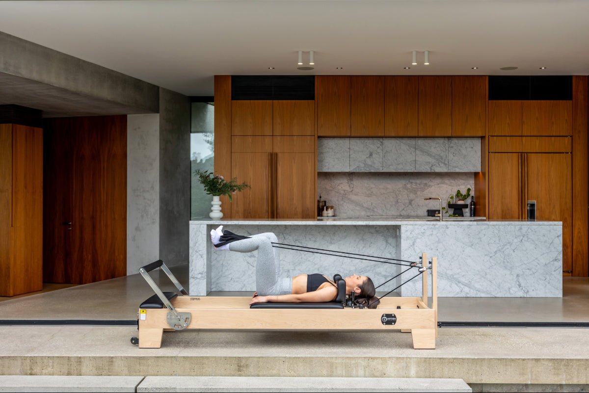 Person using light coloured wood pilates reformer with black upholstery.