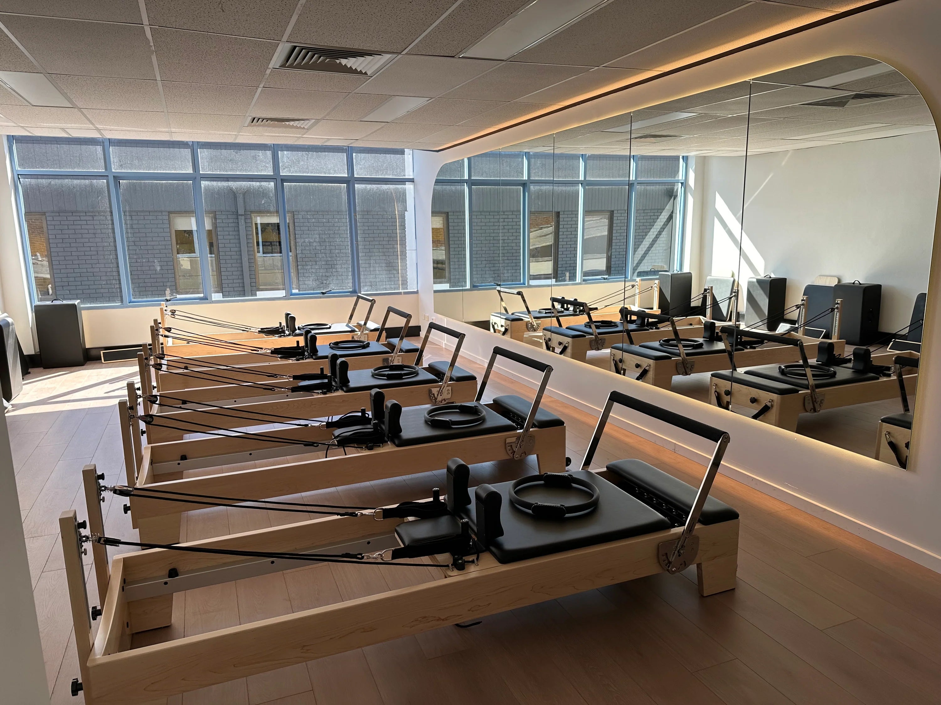 6 pilates reformers lined up in a studio in front of a mirror.
