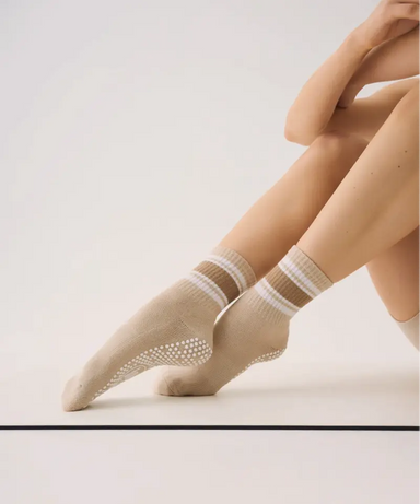 Person wearing beige grip socks with white stripes and white sole grips on a light background.