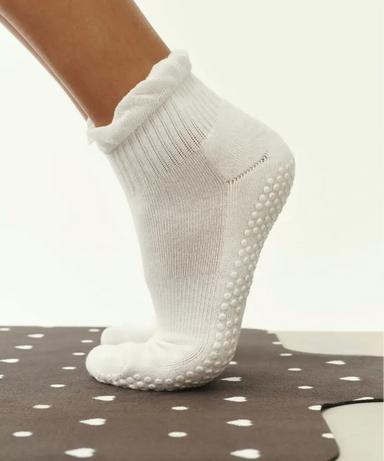 White quarter crew grip socks just above ankles with white ruffle at top, and white grips on sole.