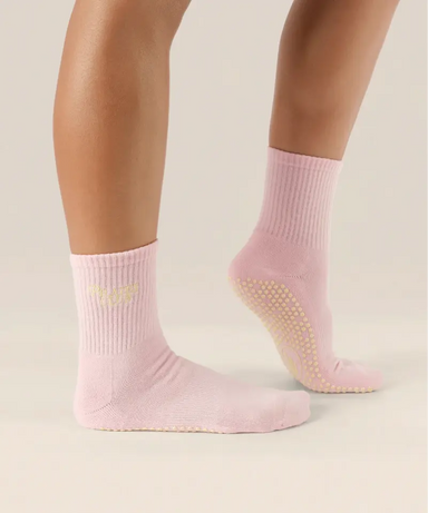 Side view of soft pink coloured crew grip socks above the ankle with "pilates club" in yellow text on the ankle and yellow grips on the sole.