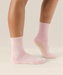Side view of soft pink coloured crew grip socks above the ankle with "pilates club" in yellow text on the ankle and yellow grips on the sole.