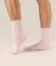 Side view of soft pink coloured crew grip socks above the ankle with "pilates club" in yellow text on the ankle and yellow grips on the sole.