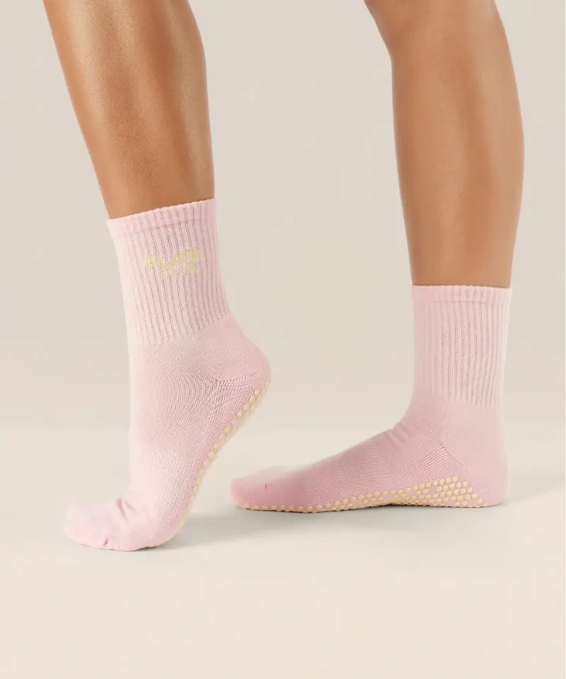 Side view of soft pink coloured crew grip socks above the ankle with "pilates club" in yellow text on the ankle and yellow grips on the sole.