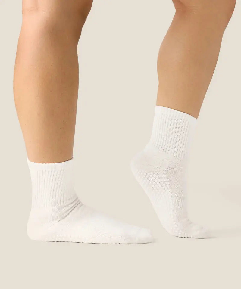 Side view of white crew grip socks above ankles with white grips on sole.