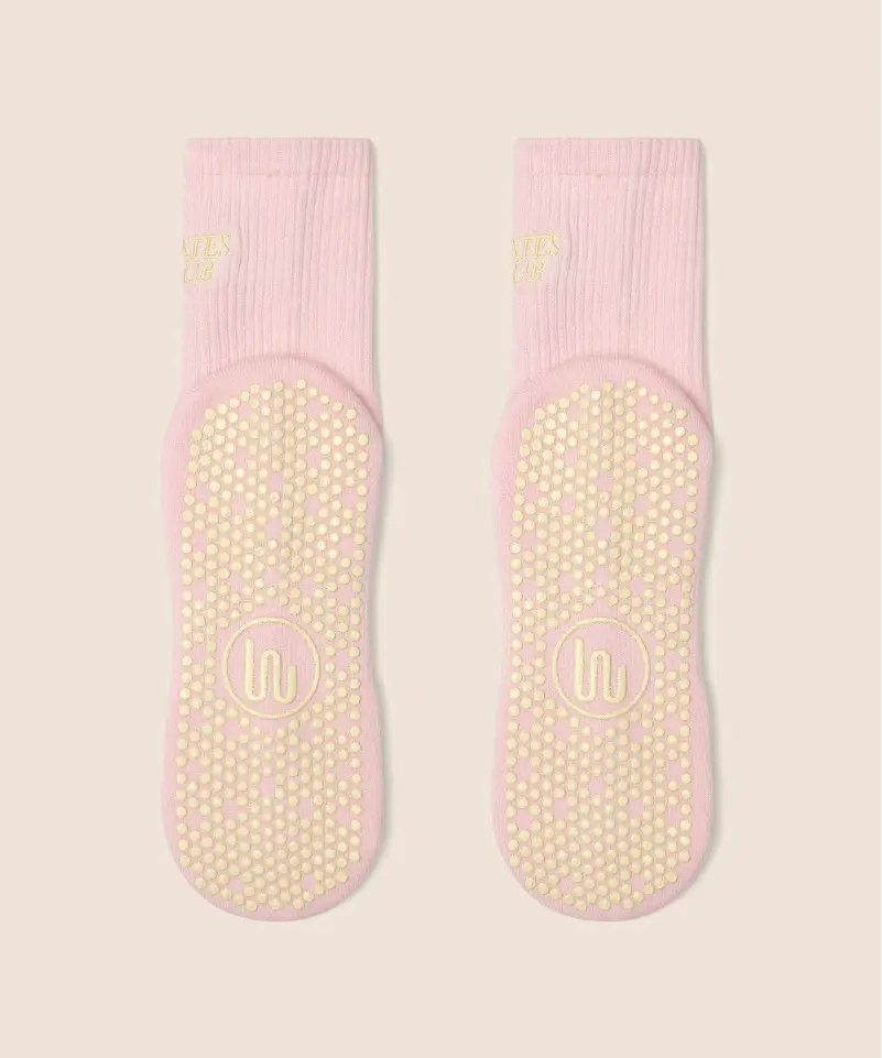 View of the sole of soft pink crew socks with yellow grips and MoveActive logo on the sole, and yellow "pilates club" text on the ankle.