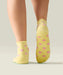 Rear view of yellow quarter crew grip socks just above ankle, with ruffle at the top, small pink flowers, and yellow grips and MoveActive logo on the sole.