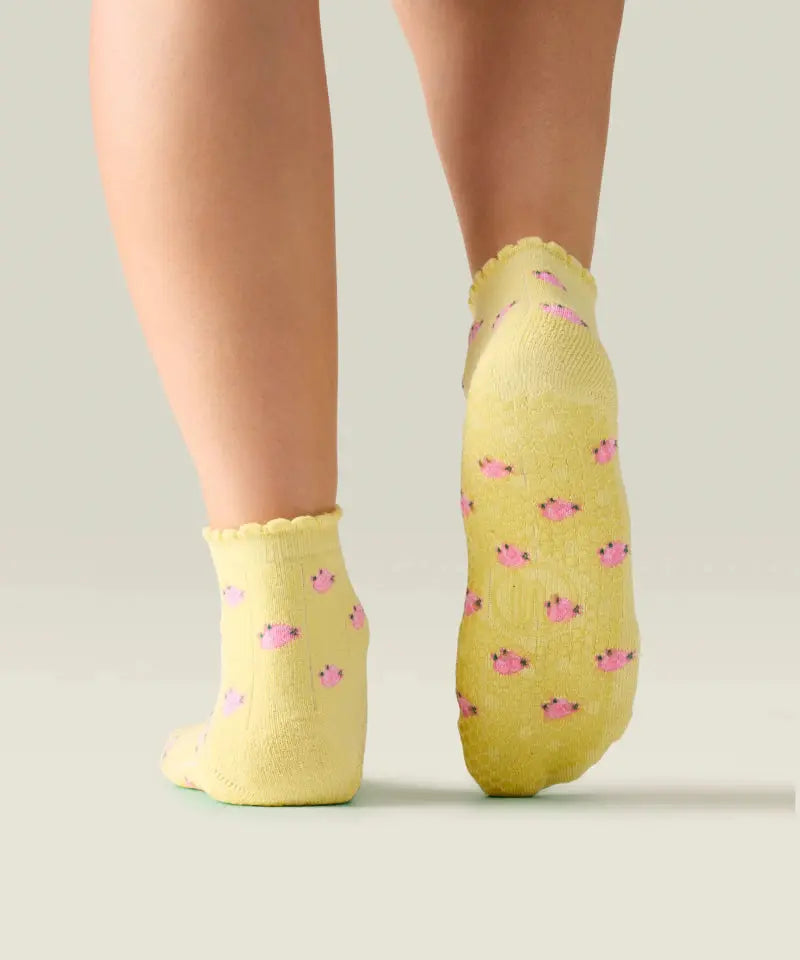 Rear view of yellow quarter crew grip socks just above ankle, with ruffle at the top, small pink flowers, and yellow grips and MoveActive logo on the sole.