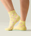Side view of yellow quarter crew grip socks just above ankle, with ruffle at the top, small pink flowers, and yellow grips and MoveActive logo on the sole.
