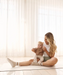 Woman sitting holding a baby on a pilates mat wearing beige grip socks with white strips and white sole grips.