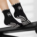 Black Elliosa dual direction grip socks in Pilates Social Club with white bow-shaped grips on the sole and 'pilates social club' embroidered around a bow.