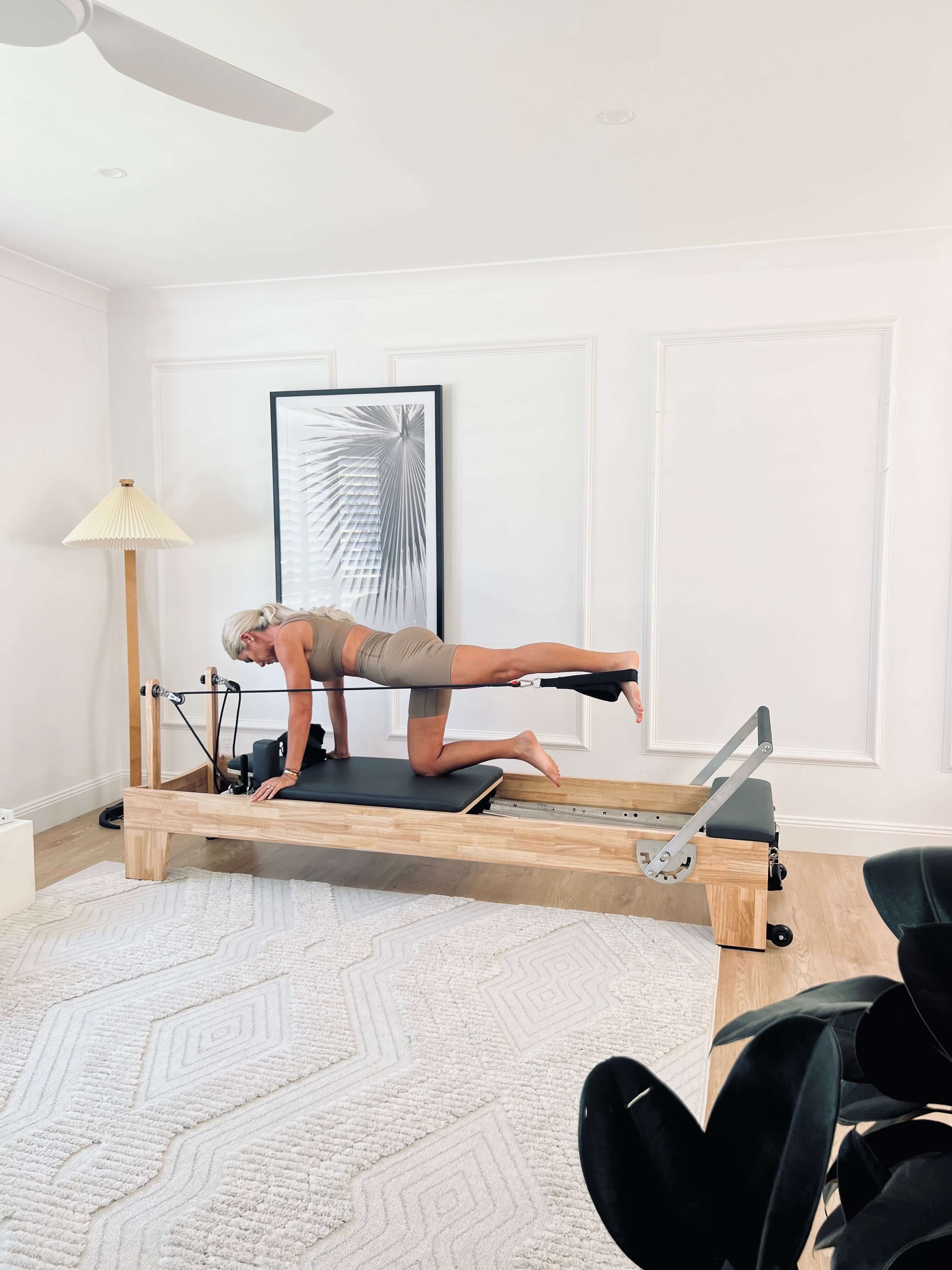 Woman exercising on the Core Collab Eco Pilates reformer in a living room setting. 