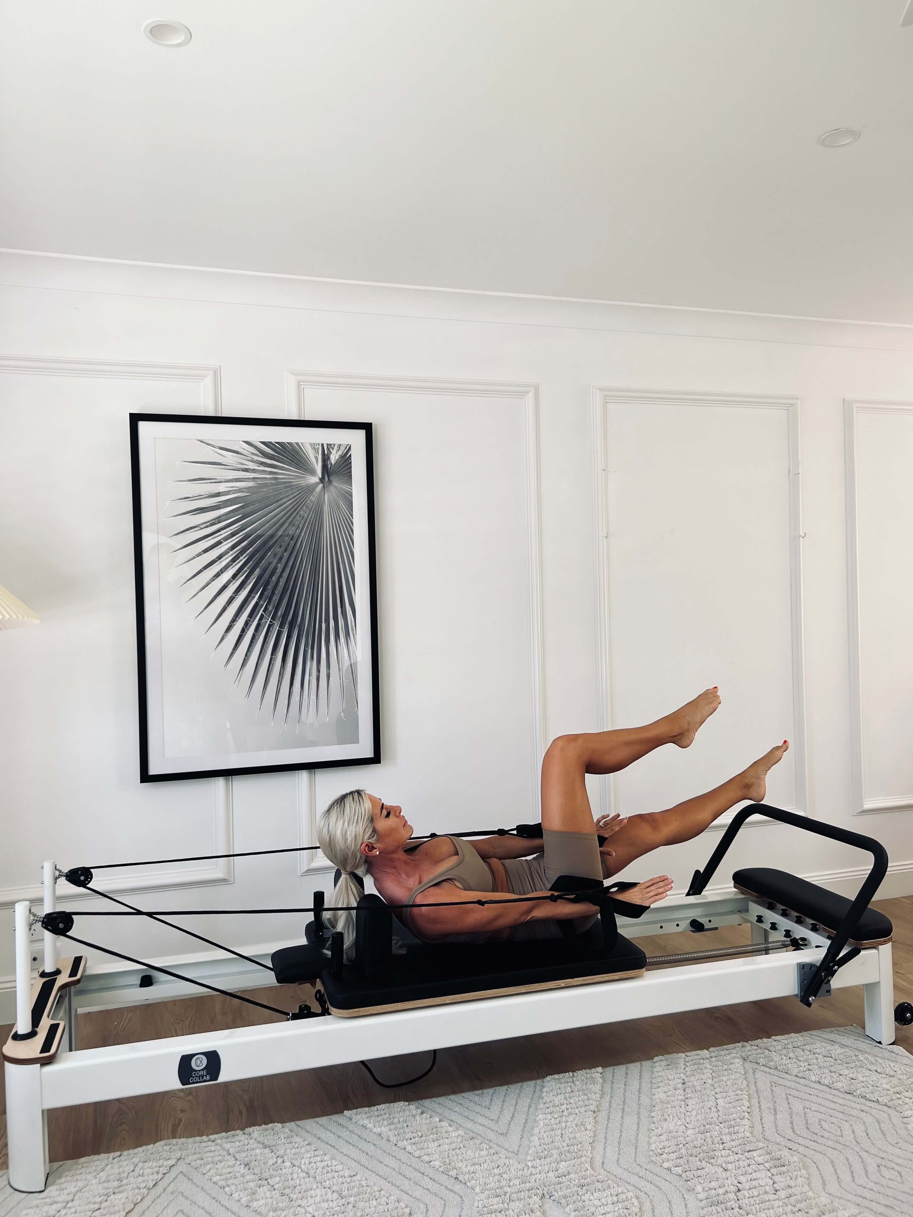 Woman exercising on the Core Collab Queen studio Pilates reformer in a living room setting.