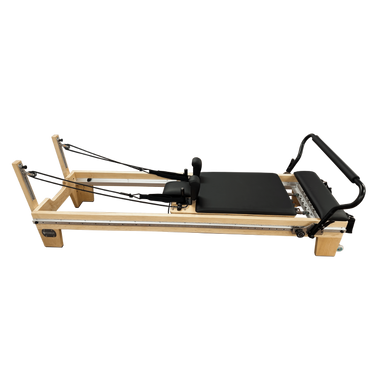 Light coloured wooden pilates reformer with black upholstery and steel track running the entire length of the reformer. 