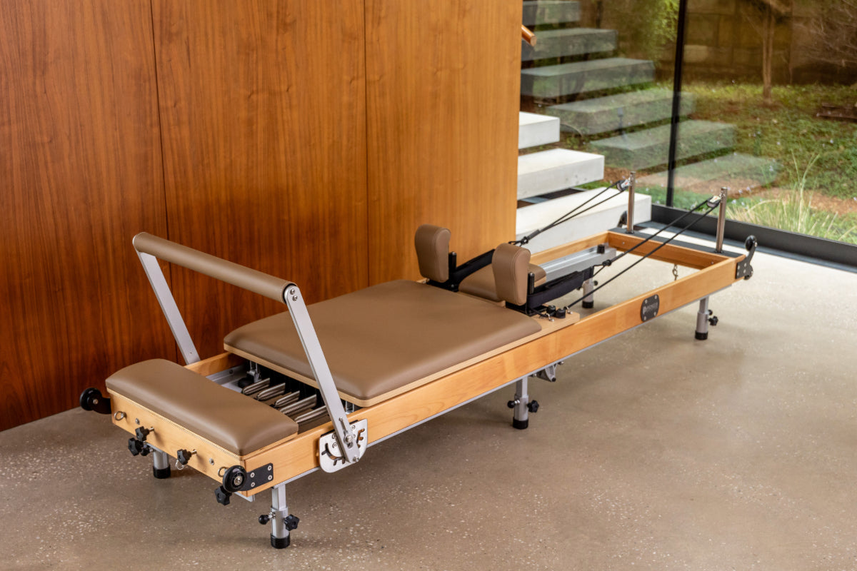 Foldable wooden reformer pilates machine with light brown upholstery, wooden frame with steel elements and black pulleys