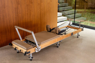 Foldable wooden reformer pilates machine with light brown upholstery, wooden frame with steel elements and black pulleys