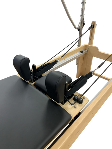 Close up of pilates reformer bed with black upholstery and trapeze attached, showing head and neck cusions.