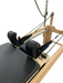 Close up of pilates reformer bed with black upholstery and trapeze attached, showing head and neck cusions.