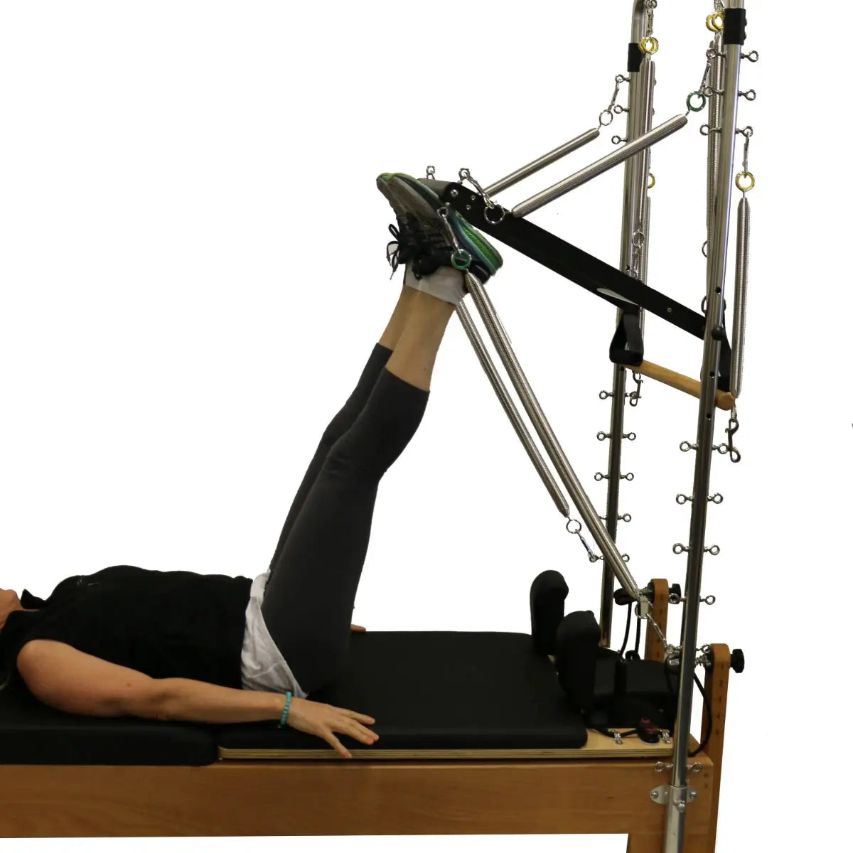 A person lying on a wooden reformer pilates table using the half trapeze attachment.