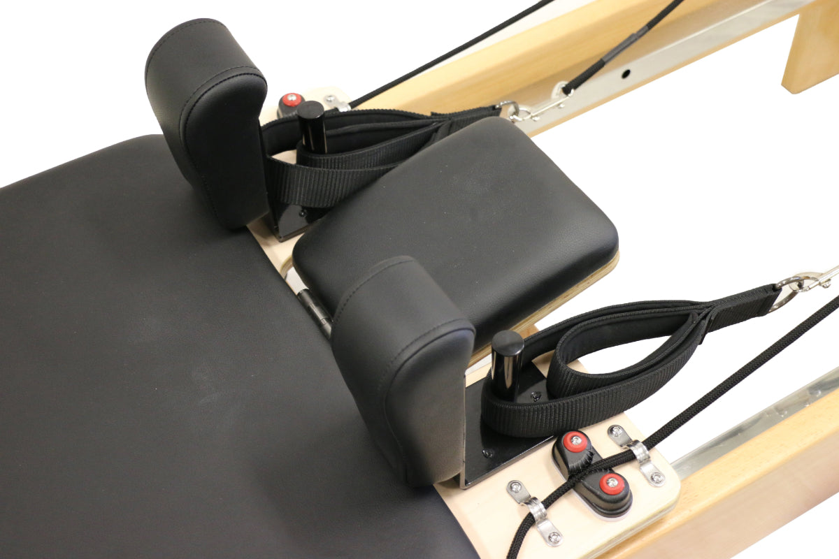 close up of reformer pilates machine with black upholstery, showing the head and shoulder cushions.