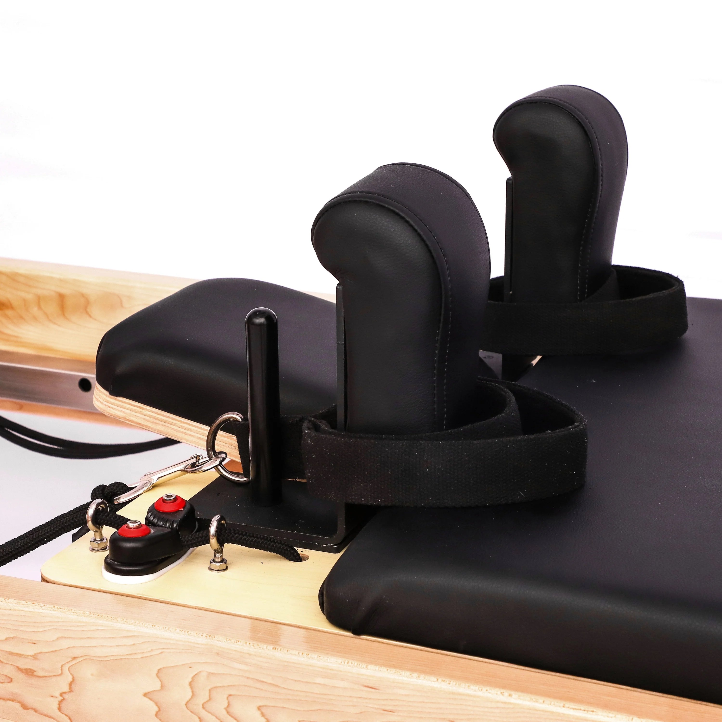 Close up of light coloured wooden pilates reformer, with black upholstery, showing head and shoulder cushions and leads.