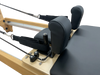 Close up of a pilates reformer machine with wooden frame and black cushioned seat showing the head and shoulder rest and ropes.