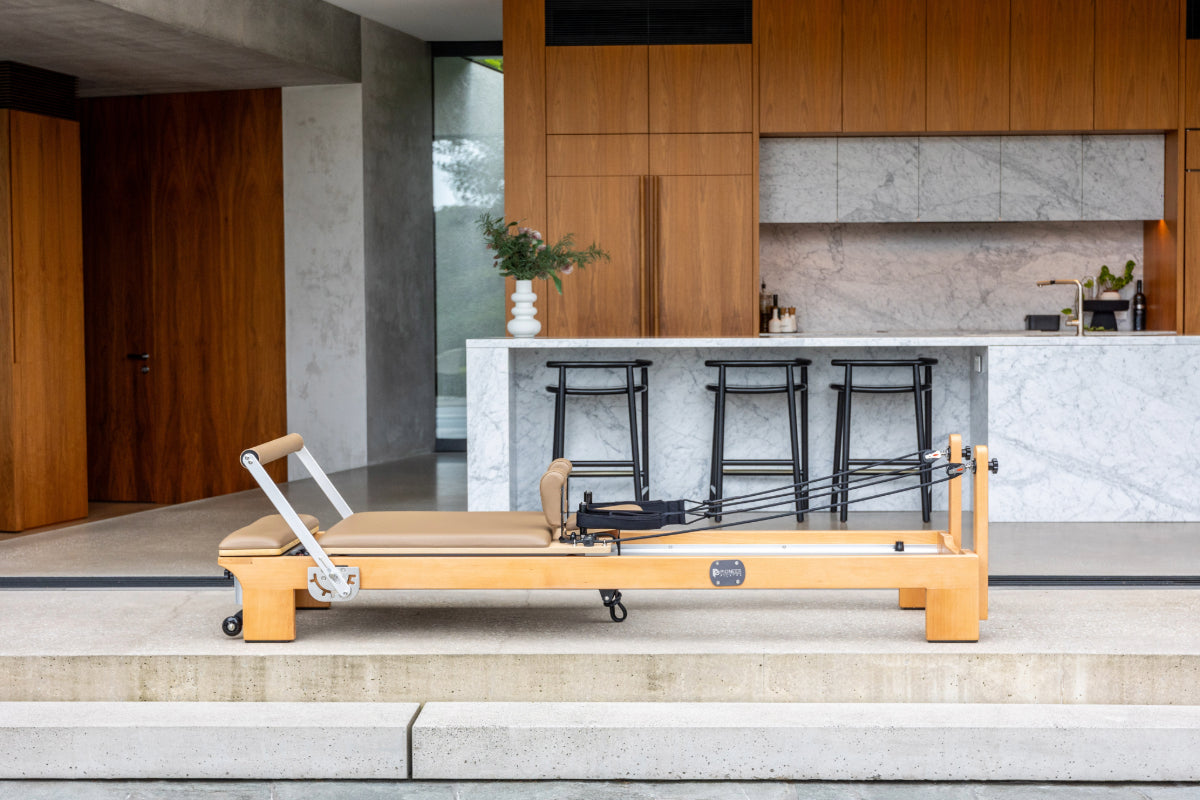 Wooden reformer pilates machine with light brown upholstery and light wood in a modern home setting