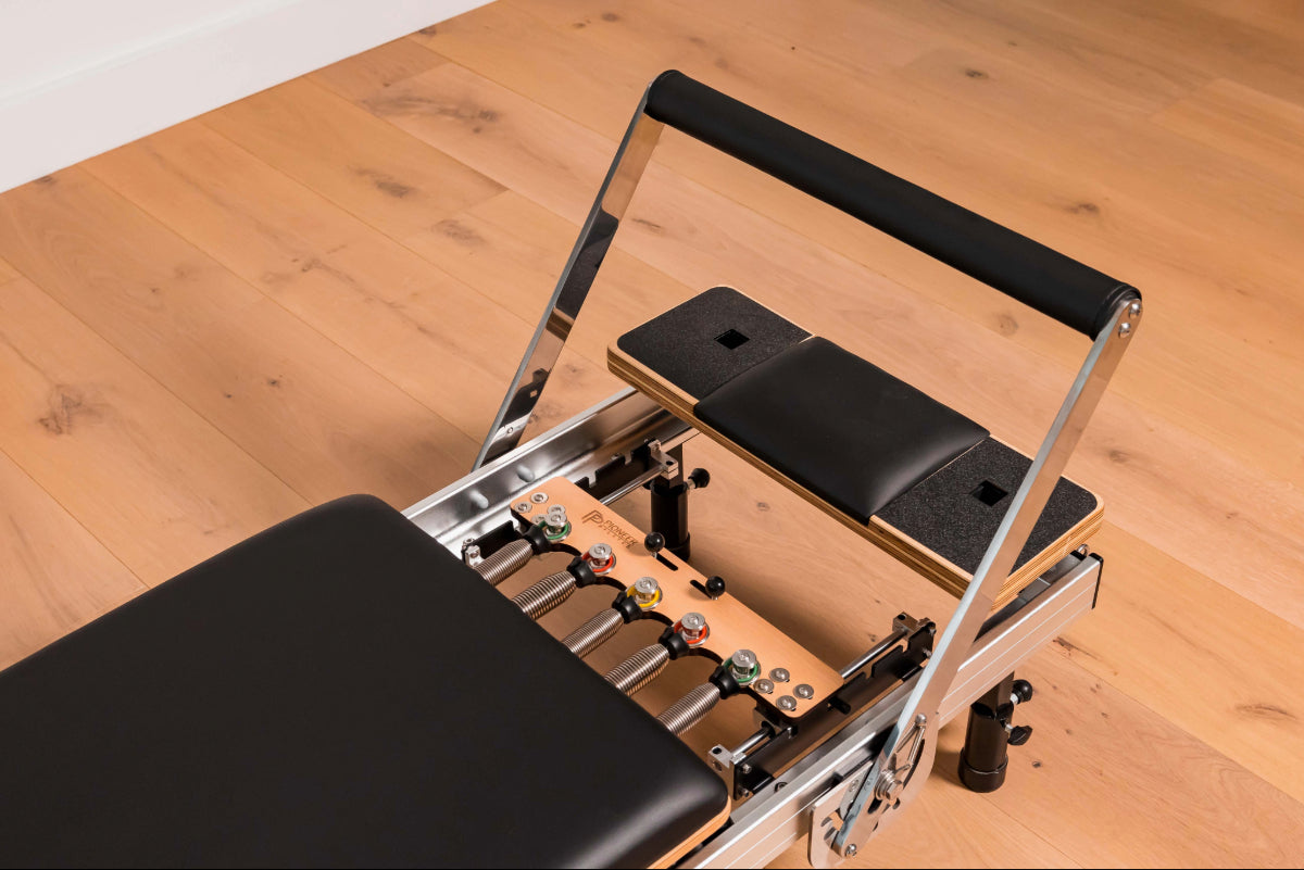 Close up of a pilates reformer machine showing 5 colour coded springs and black upholstery.