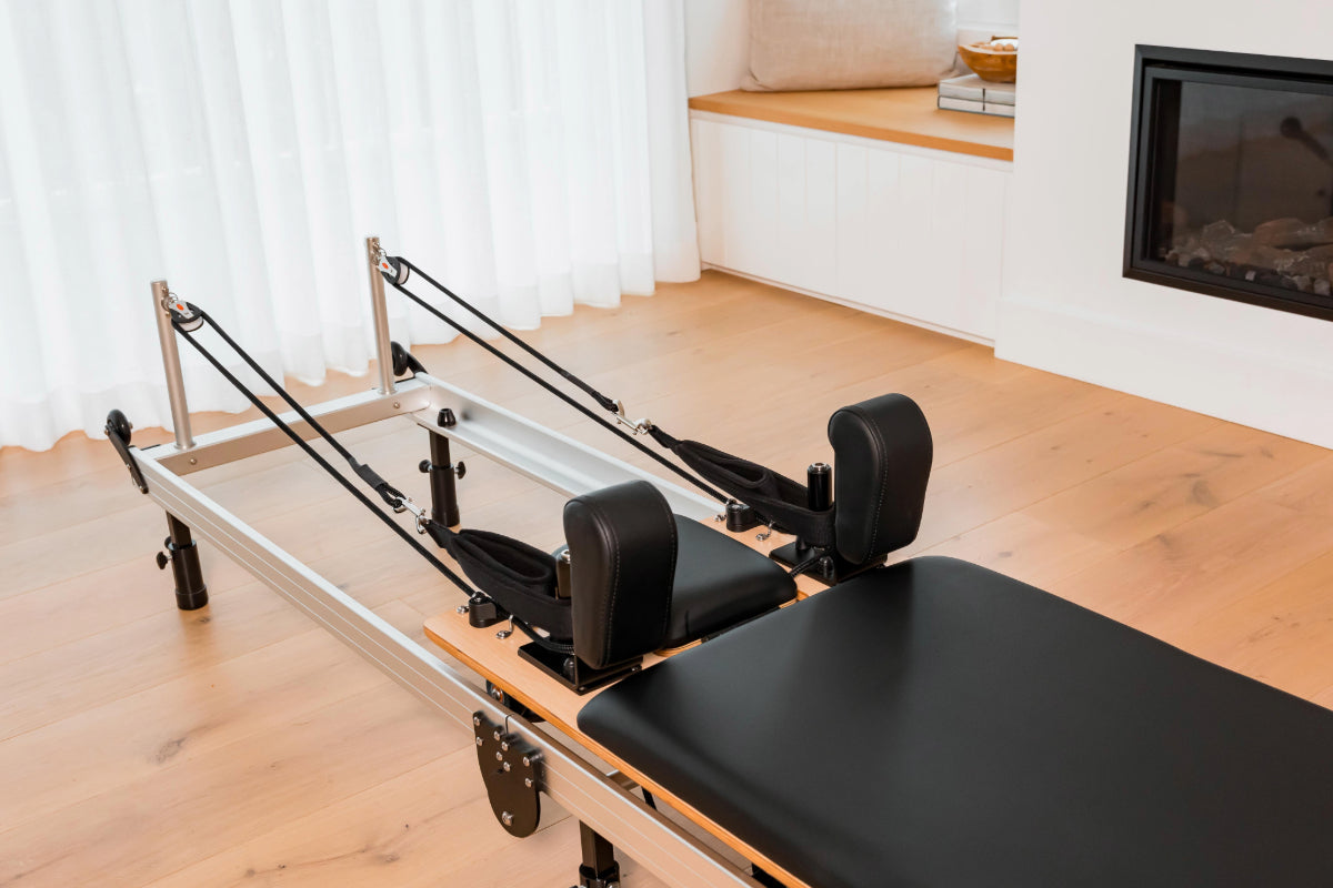 Foldable metal pilates reformer machine in a home setting with black upholstery, showing a close up of the ropes.
