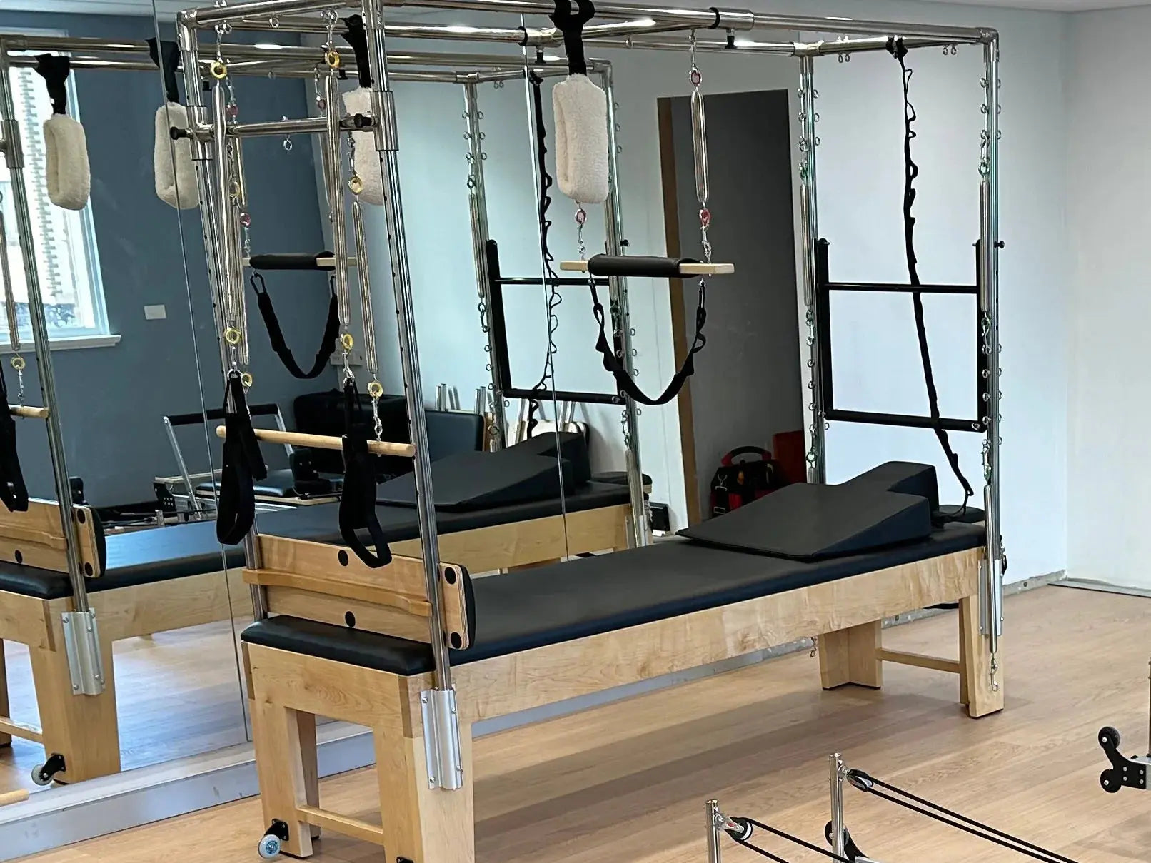 Full cadillac trapeze table in studio setting in front of a mirror, with black upholstery and wedge sitting at the head end of the table.