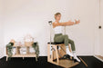 Woman sitting on a Premium Pilates Wunda Chair in a small studio.
