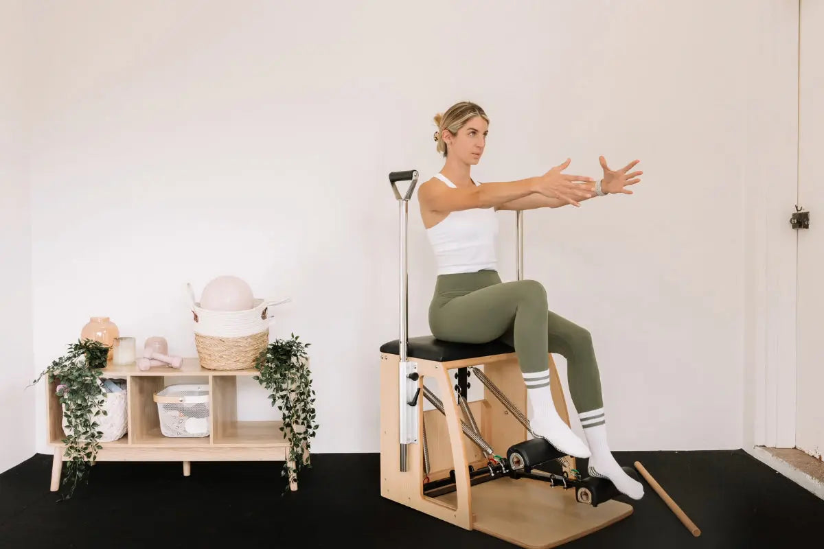 Woman sitting on a Premium Pilates Wunda Chair in a small studio.