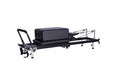 Premium fold lite Pilates reformer machine with black padded carriage and frame, silver metal guide rails, and black handlebar, shown with sitting box (not included) on a plain white background.