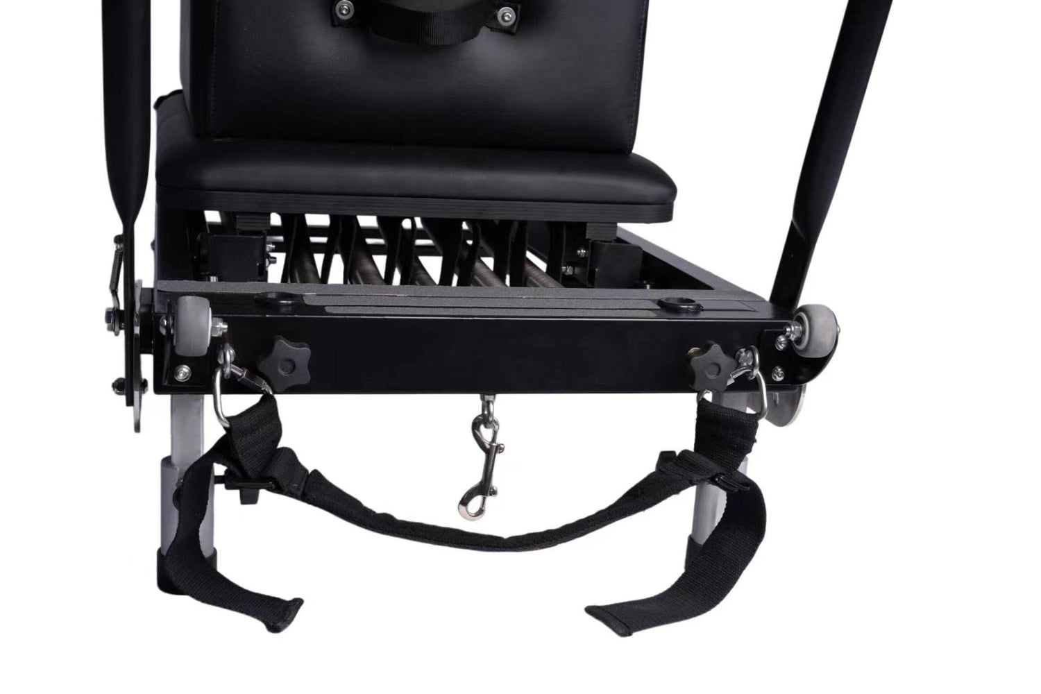 Close-up of a black Pilates reformer with a metal frame, straps, and a hanging hook, shown on a white background.
