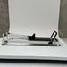Side view of the Core Collab Queen 2.0 Pilates reformer with white frame and black upholstery in white background.