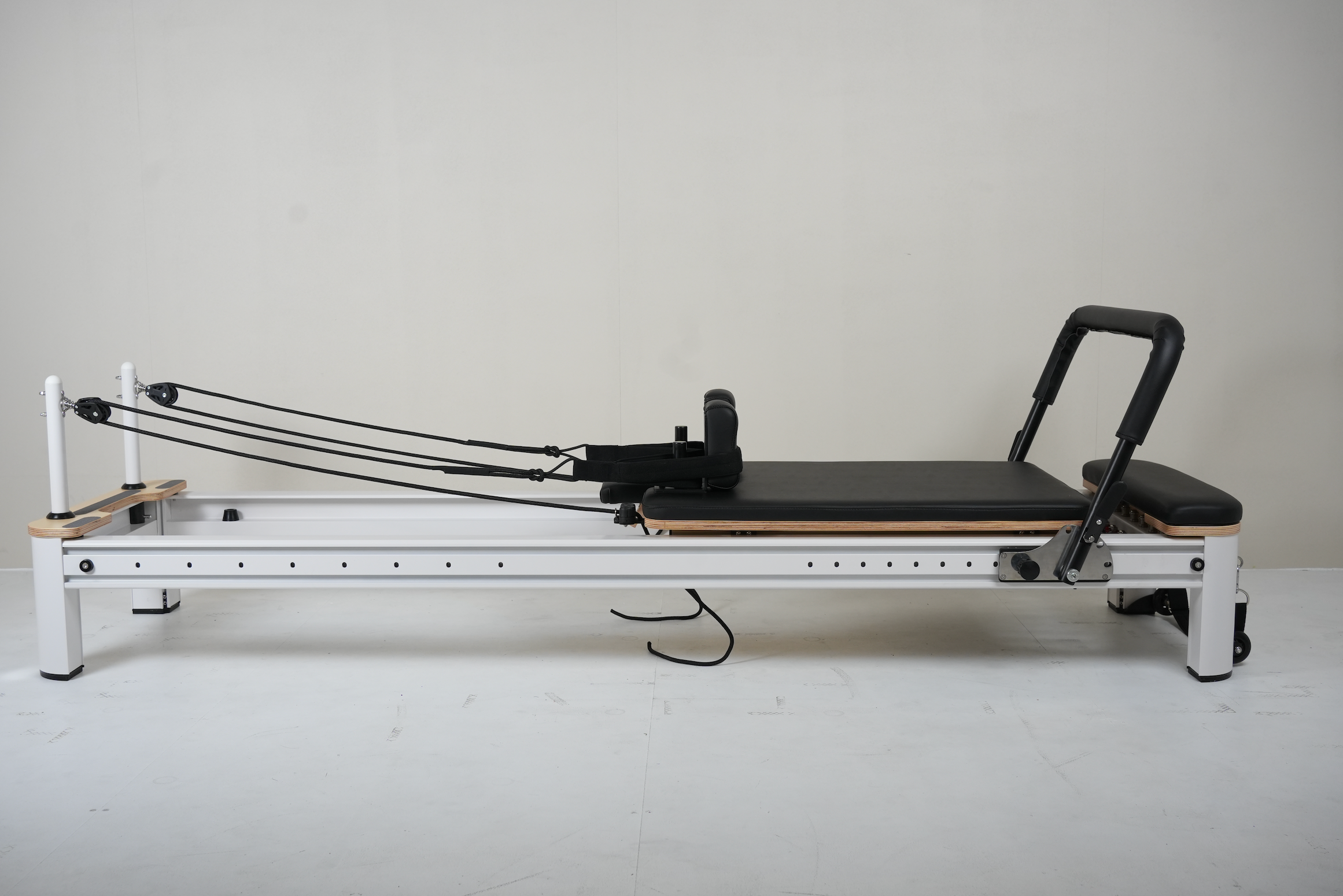 Side view of the core Collab Queen Pilates reformer showing black upholstery and white metal frame.