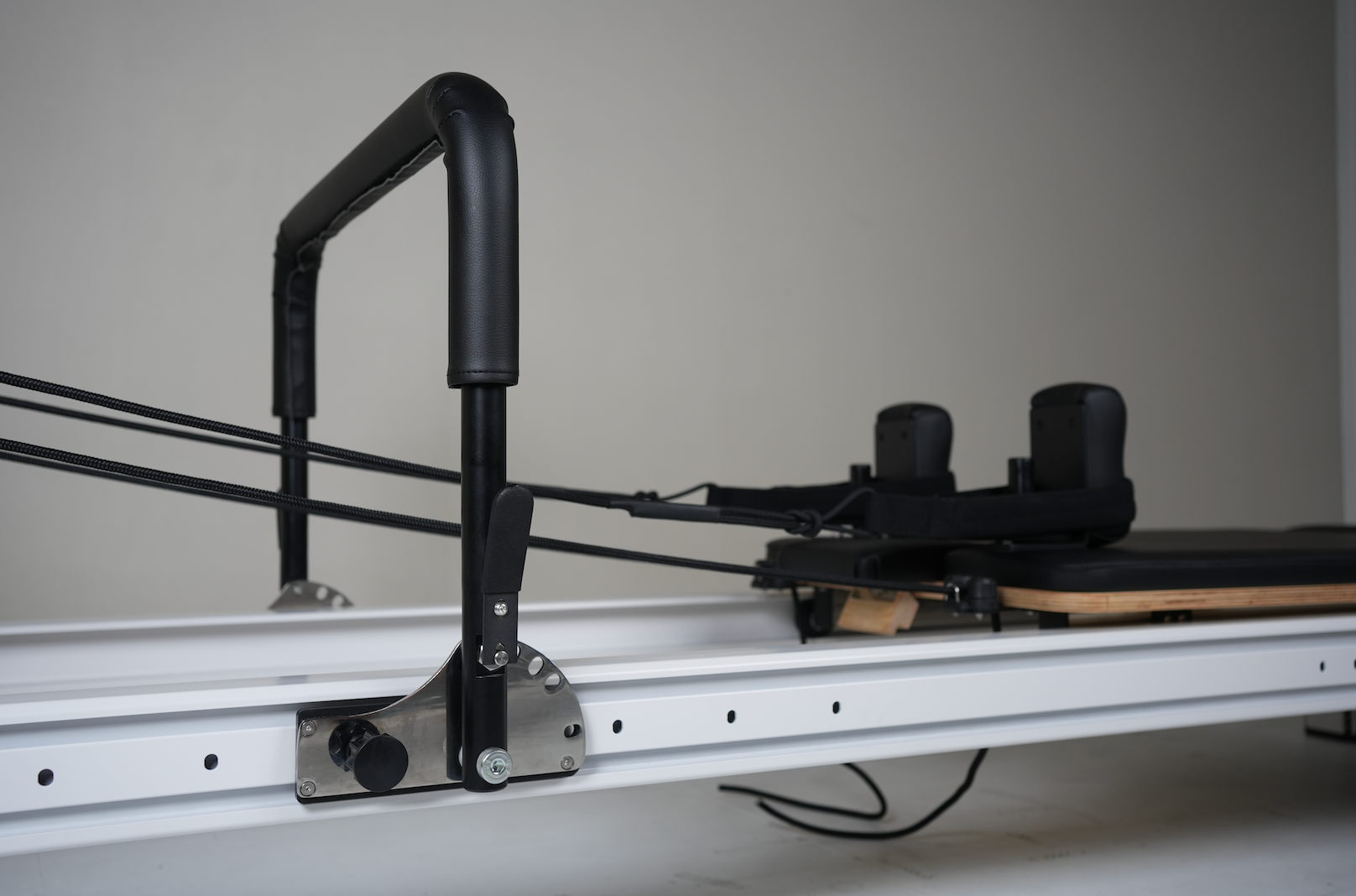 close of up the core collab queen reformer frame showing the foot bar in the middle of the white frame and the black shoulder pads and straps.