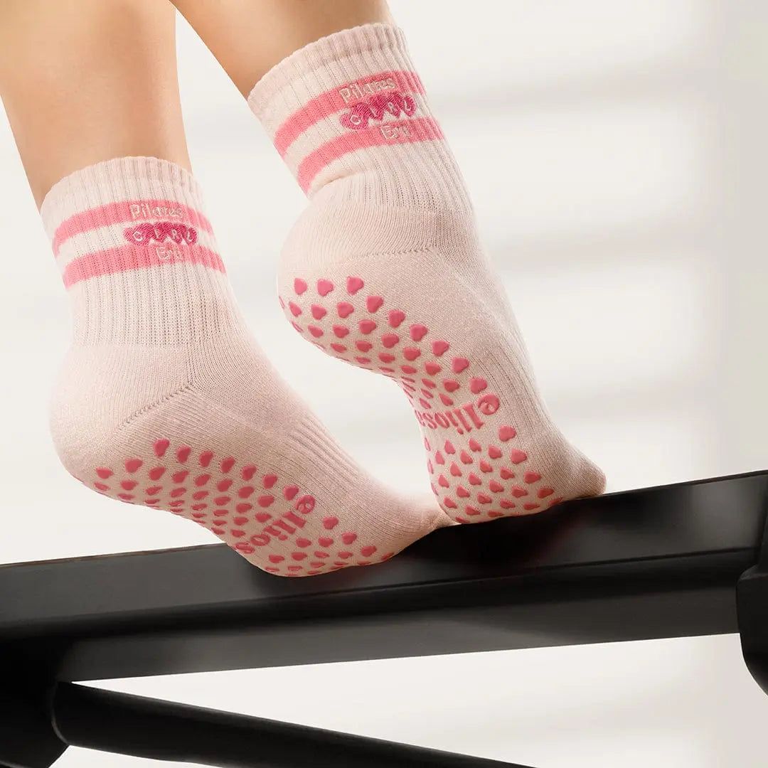Pink socks with pink heart shaped grips on the soles, with the words 'pilates girl era' embroidered on the ankles.