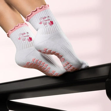 White socks with pink ruffles and the words "pilates princess" emrboidered with pink images, and pink bow shaped grips on the soles.