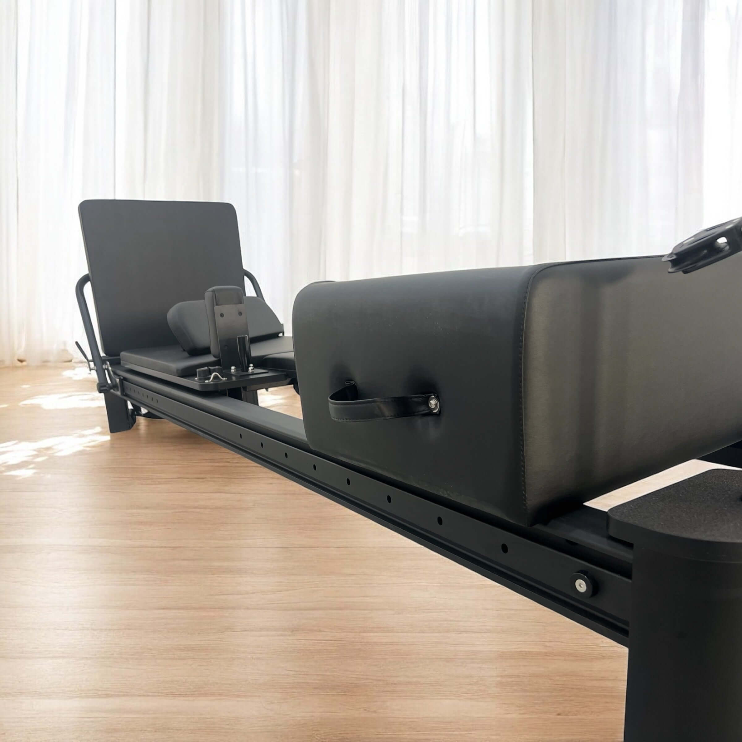 angle view of the core collab queen Pilates reformer in black frame and black upholstery with jumpboard and sitting box.